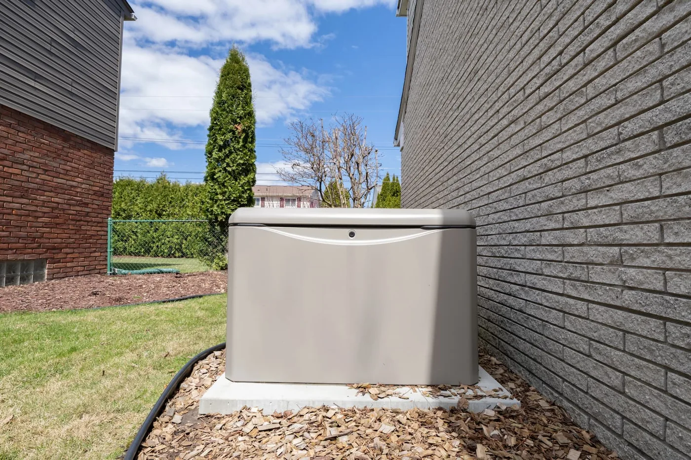 A Generac standby generator on a concrete pad in a side yard, set off the brick wall with service clearance and kept out of the front yard.